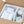 Open cardboard shipping box containing a white electronic device wrapped in plastic, a printed user manual, and accessories in clear bags on white foam insert.